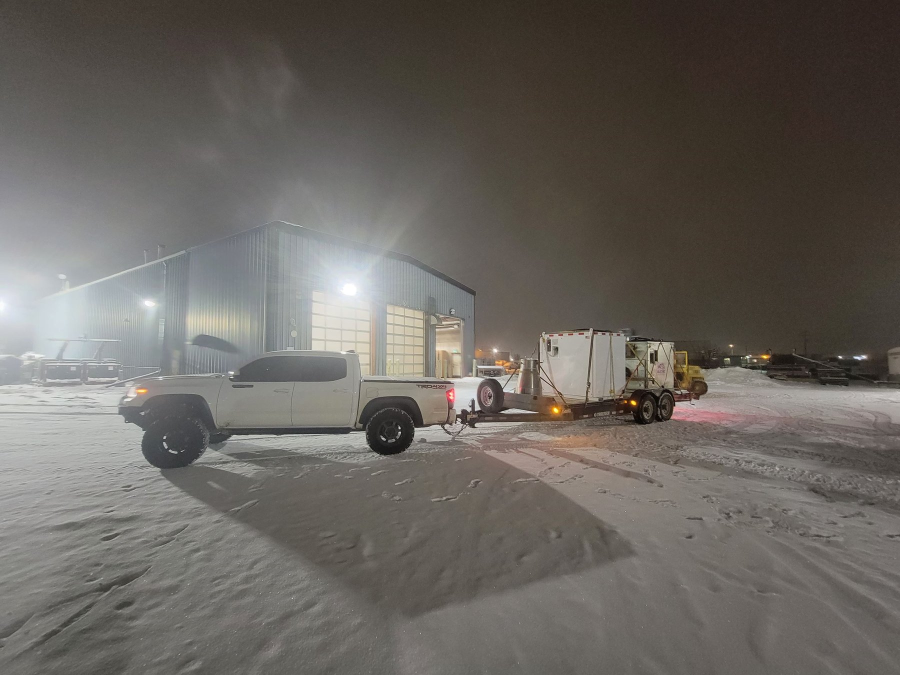 Hotshot truck with trailer delivering equipment to an industrial site at night